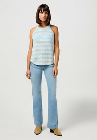 Top de alças listrado azul claro com textura canelada, apresentando um decote redondo. Combinado com jeans azul claro de perna larga e botas de tornozelo em tom bege.