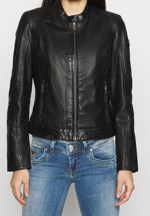 Person iført en tætsiddende sort læderjakke med lynlås foran og lynlåslommer, kombineret med blå jeans.