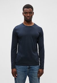 Mørkeblå langermet t-skjorte laget av mykt stoff med rund hals og figursydd design, parret med slitte blå denimjeans.