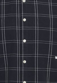 Camisa de cuadros de color azul marino, confeccionada en algodón, con líneas de cuadrícula blancas, dos bolsillos en el pecho y botones planos.