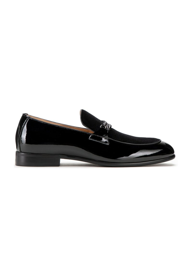 Zwarte gepatineerde leren loafers met een zachte zwarte suède neus en een decoratieve metalen accent. Heeft een lage hak en een ronde vorm.