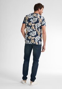 Valkoinen kukallinen lyhythihainen paita, jossa on tummansinisiä suuria lehtiä ja kukkia, yhdistettynä tummiin farkkuihin ja valkoisiin lenkkareihin.