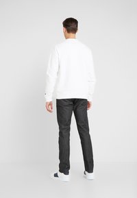 White sweatshirt with a round neck, paired with dark denim pants. The outfit is completed by white sneakers with navy accents.