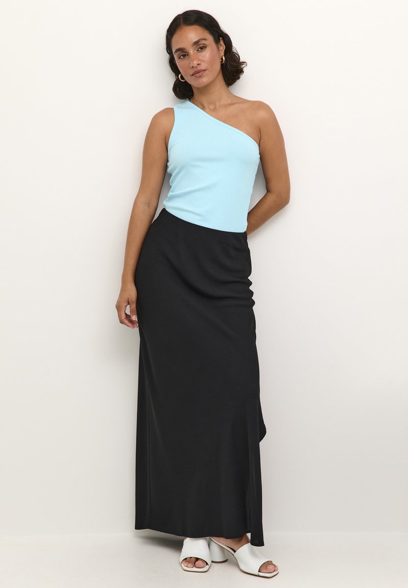 Top de un hombro en azul claro acanalado combinado con una falda maxi negra, que presenta una abertura lateral, y sandalias de tacón abierto blancas.