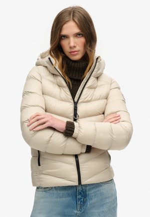 Beige pufferjack met een capuchon, met een gewatteerd ontwerp, een rits aan de voorkant en geribbelde bruine gebreide manchetten. Draagt over een gestructureerde trui.