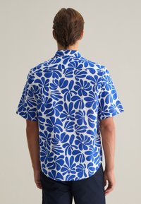 Camisa de manga corta con un patrón floral en azul y blanco, fabricada en tejido suave y con un dobladillo recto y una yugo trasero curvado.