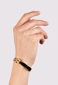 Black enamel bangle bracelet with a gold hardware accent and a diamond-encrusted detail, worn on a hand with manicured nails.