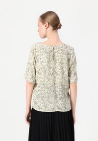 Lys grønn blomsterbluse med korte ermer, med knappelukking på baksiden og et lett strukturert stoff.