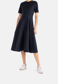 Marineblaues A-Linien-Kleid mit kurzen Ärmeln, rundem Ausschnitt und vertikalen Nähten, kombiniert mit hellgrauen Sneakers mit orangefarbenen Akzenten.