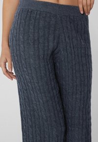 Donkergrijze kabelgebreide broek met een brede elastische tailleband, voorzien van een geribbelde textuur en verticale patronen voor een gezellige uitstraling.