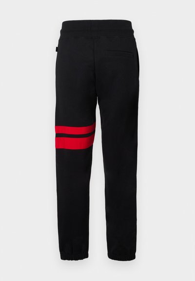 Czarne dresy o slim fit, z dwoma czerwonymi poziomymi paskami na lewym nogawce, elastyczną talią i ściągaczami przy nogawkach.