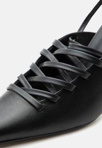 Μαύρο παπούτσι με μυτερή μυτούλα, πολλαπλές διασταυρούμενες δερμάτινες λουρίδες στο πάνω μέρος και λεπτό λουράκι στον αστράγαλο.