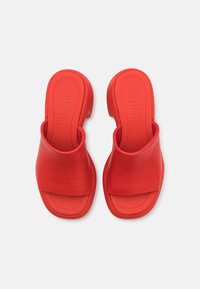Chinelas deslizantes de couro vermelho com uma tira larga, palmilha contornada e um salto baixo. Textura suave com o logótipo embossado na palmilha.