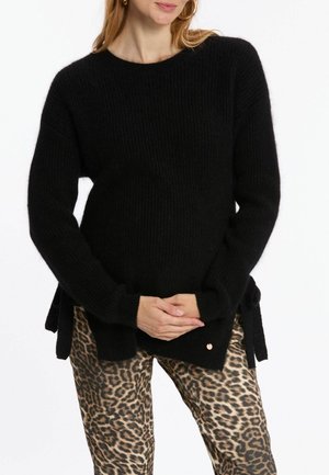 Zwarte geribde trui met een ronde halslijn, lange mouwen en zijsplitsingen; gecombineerd met leggings met luipaardprint die een glanzende textuur hebben.