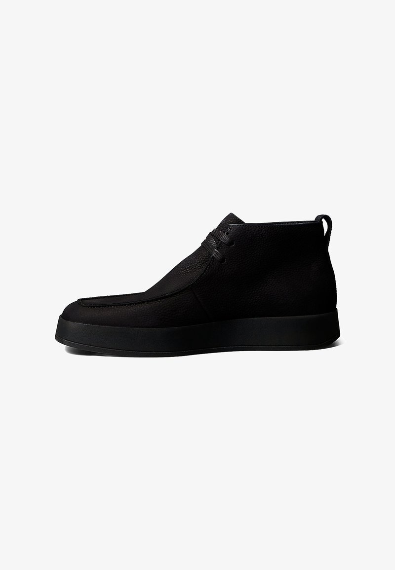 Chaussure décontractée mi-montante en cuir noir avec fermeture à lacets et semelle plate en caoutchouc sur fond blanc.