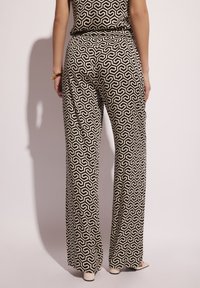 Czarne i beżowe spodnie z wysokim stanem i szerokimi nogawkami w geometryczny wzór. Gładki materiał z lekko układającym się krojem. Ukryty detal w postaci kieszeni.