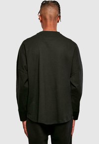 Schwarzes Langarm-T-Shirt mit Rundhalsausschnitt, entspannter Schnitt und überschnittenen Schultern. Glattes Baumwollgewebe mit abgerundetem Saum.