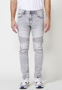 Denimjeans lavet af lys grå stof, med ribbede detaljer ved knæene, slim fit og fem-lomme design. Båret med hvide sneakers.