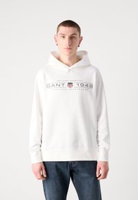 Felpa bianca con cappuccio caratterizzata da un logo frontale con "GANT 1949" e righe. Realizzata in un materiale morbido con una vestibilità comoda e maniche lunghe.