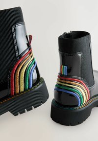 Botas negras hasta el tobillo con un eje de tela texturizada. El tacón presenta rayas bordadas multicolores y un lazo lateral para facilitar su colocación.