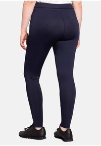 Navy leggings made from stretchy material, featuring a high waistband and a fitted silhouette. Worn with black athletic shoes.