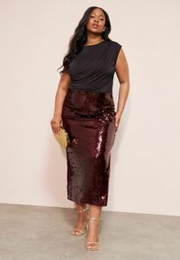 Černý top bez rukávů s draped detailem, spárovaný s flitrovou burgundskou tužkovou sukní. Zlaté akcenty zahrnují psaníčko a sandály na podpatku.