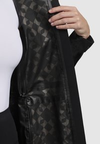 Black jacket with a geometric patterned interior. Smooth fabric exterior and textured lining. Includes a drawstring and hidden pockets.