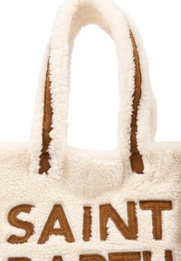 Borsa a tote cremosa e soffice con dettagli in pelle marrone. Presenta una forma rettangolare e manici spessi e texturizzati. Le lettere "SAINT" sono ricamate in modo prominente.