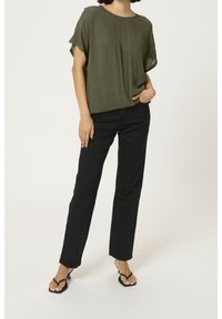 Top verde oliva a maniche corte con una vestibilità rilassata, abbinato a jeans neri a vita alta e sandali nero con fascia, creando un outfit casual.