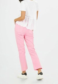 Pantalons en coton rose avec une coupe droite et un ourlet effiloché, associés à un haut blanc présentant un design superposé en broderie anglaise au niveau de la taille. Baskets blanches.