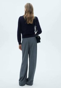 Marineblauwe trui, wolblend, getailleerd bij de taille; grijze, gestreepte broek, wijde pijpen; zwarte handtas, leer, over de schouder gedragen.