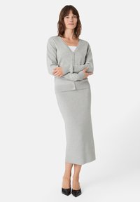 Šedý pletený kardigan s výstřihem do V a zapínáním na knoflíky, zkombinovaný s přiléhavou midi sukní. Součástí soupravy je měkká textura. Černé špičaté podpatky.