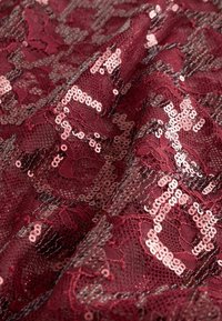 Burgundi csipkeanyaga, amely flitterekkel díszített virágmintás, texturált felülettel és finom, részletes kidolgozással.