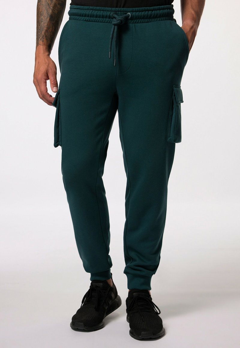 Teal Jogginghosen mit einem Kordelzugbund, seitlichen Cargo-Taschen und schmal zulaufenden Bündchen, aus weichem, glattem Stoff. Kombiniert mit schwarzen Sneakers.