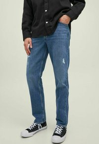 Jeans de mezclilla azul claro con detalles desgastados, diseño de pierna recta y bolsillos laterales, combinados con zapatillas de lona en blanco y negro.