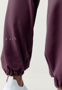 Bordeauxfärgade sweatpants med elastiskt avslut, med en sydd söm och en subtil logodetalj i grått på benet. Bärs med vita sneakers.