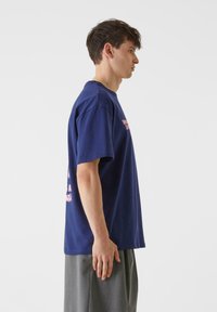 Marinblå bomullströja med korta ärmar, med rosa text på framsidan och baksidan, visad från sidan, med en lös passform.