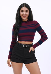 Long-sleeve cropped sweater in dark red and navy stripes, ribbed texture. Paired with high-waisted black shorts and a black belt.