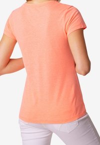 Camiseta de manga corta en un vibrante color coral, hecha de una tela suave con un ajuste relajado y una textura lisa, mostrando la vista posterior.