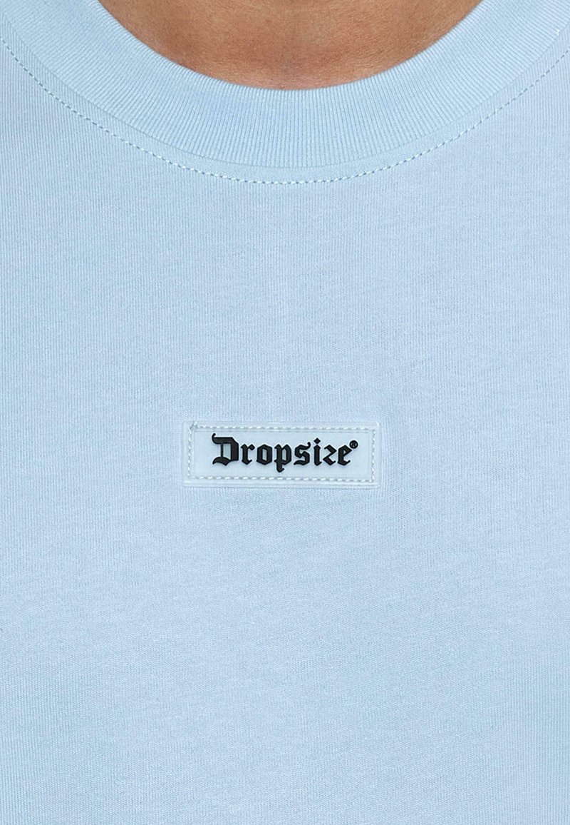 Lyseblå T-shirt lavet af blødt stof, med en ribbet rund hals og et sort mærke syet ind i forsiden med ordet "Dropsize."