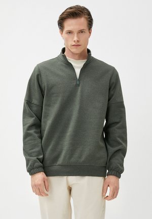 Mørkegrøn kvart-zip sweatshirt med en tekstureret overflade, elastiske manchetter og en høj krave, parret med lysebeige bukser.
