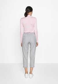 Lichtroze slim-fit coltrui, vergezeld van grijze cropped broeken met een elastische tailleband en twee achterzakken, gecombineerd met witte sneakers.