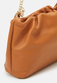 Sac à main en cuir souple couleur fauve avec un design froncé et une bandoulière chaîne dorée, montré en gros plan sur fond blanc.