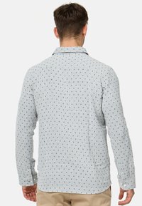 Camisa de manga larga azul claro con un sutil patrón geométrico, cuello abotonado y mangas con puños, hecha de una tela texturizada.