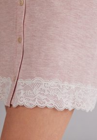 Ljusrosa kjol med knappfront och intrikat vit spetsdetalj vid kanten. Tyget har en mjuk, texturerad yta.