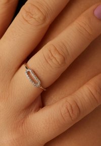 Zilveren ring met een langwerpig ovale vorm, met een rij kleine sprankelende stenen langs de bovenkant. Draagt op een hand met een gestructureerde huid.
