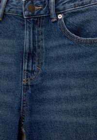 Gros plan sur l'avant d'un jean en denim bleu avec bouton, fermeture éclair, rivet de la petite poche, et détails de couture orange.