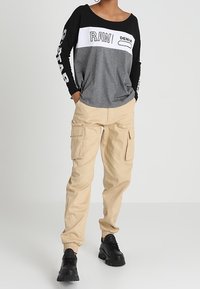 Svart, grå och vit långärmad skjorta med grafisk text; tanfärgade cargobyxor med elastiska muddar; svarta kraftiga sneakers.