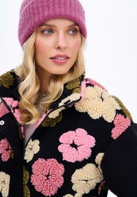 Fleecová bunda s černým základem zdobená texturovanými květinovými vzory v růžové, krémové a zelené barvě. Doplněna růžovou žebrovanou čepicí.