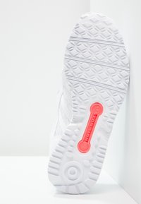 Vit sportskosula med texturerat gummi grepp. Har en framträdande korallfärgad "TORSION"-detalj och upphöjda mönster för bättre grepp.